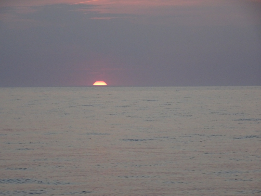 Couché de soleil sur mer calme. seul un tout petit secteur de soleil orange est encore visible sur l'horizon.