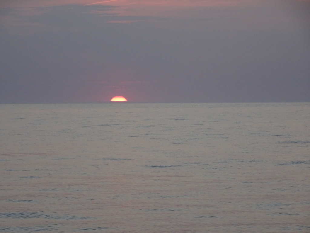 Couché de soleil sur mer calme. seul un tout petit secteur de soleil orange est encore visible sur l'horizon.